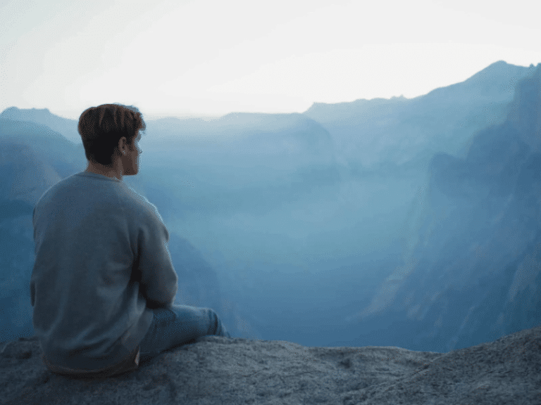 Man sitting on a rock enjoying a peaceful mountain view, symbolizing mindfulness and relaxation